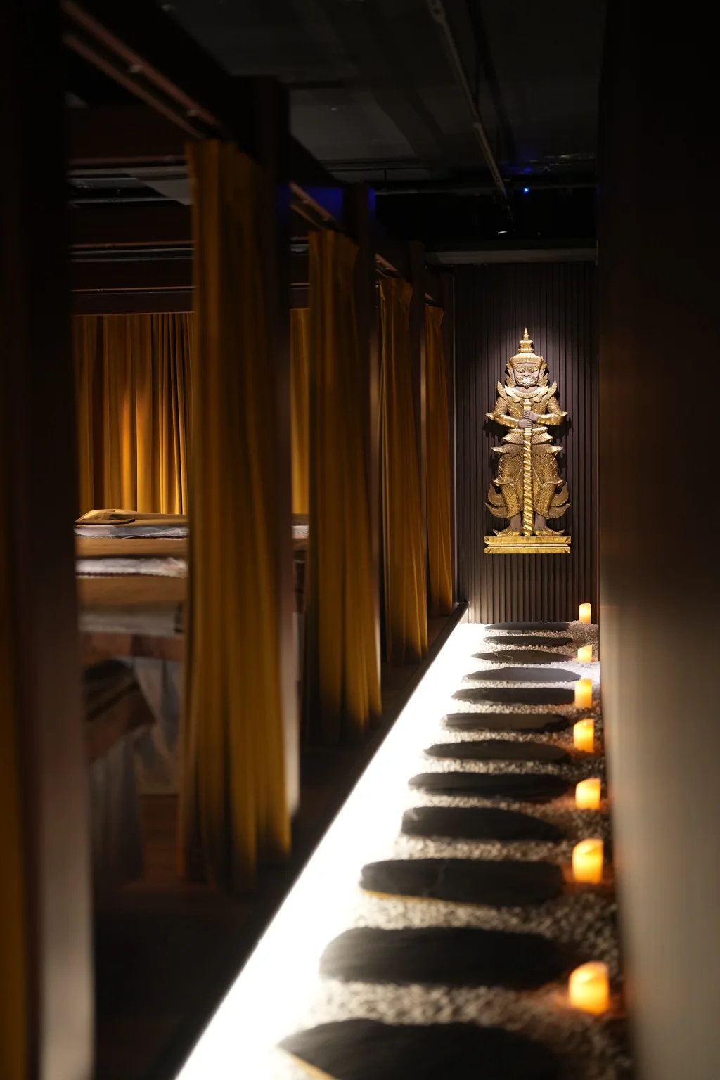 Candlelit corridor at Kwun Tong with a Thai Yaksha statue at the far end and curtained treatment bays on the left